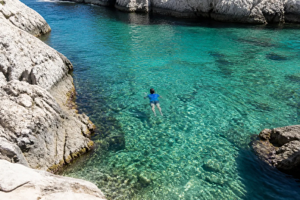Rochers et eau claire d&rsquo;une calanque avec un nageur en tee-shirt anti-UV en surface