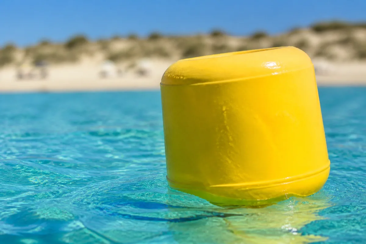Bouée jaune de chenal balisé en mer avec la plage en arrière-plan
