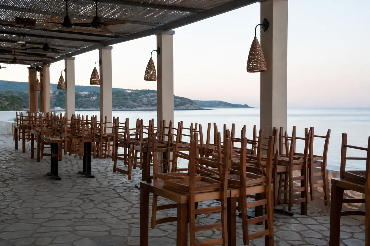 Terrasse de restaurant en bord de mer préparée avant le service, chaises alignées et lumière du matin